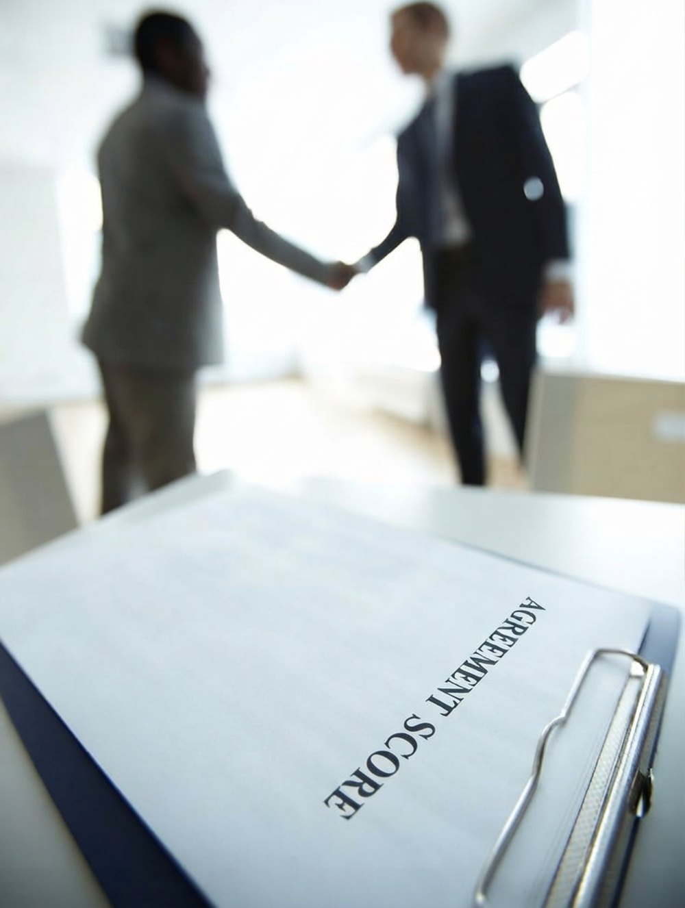 A clipboard headed Agreement Score with two people shaking hands out of focus behind it