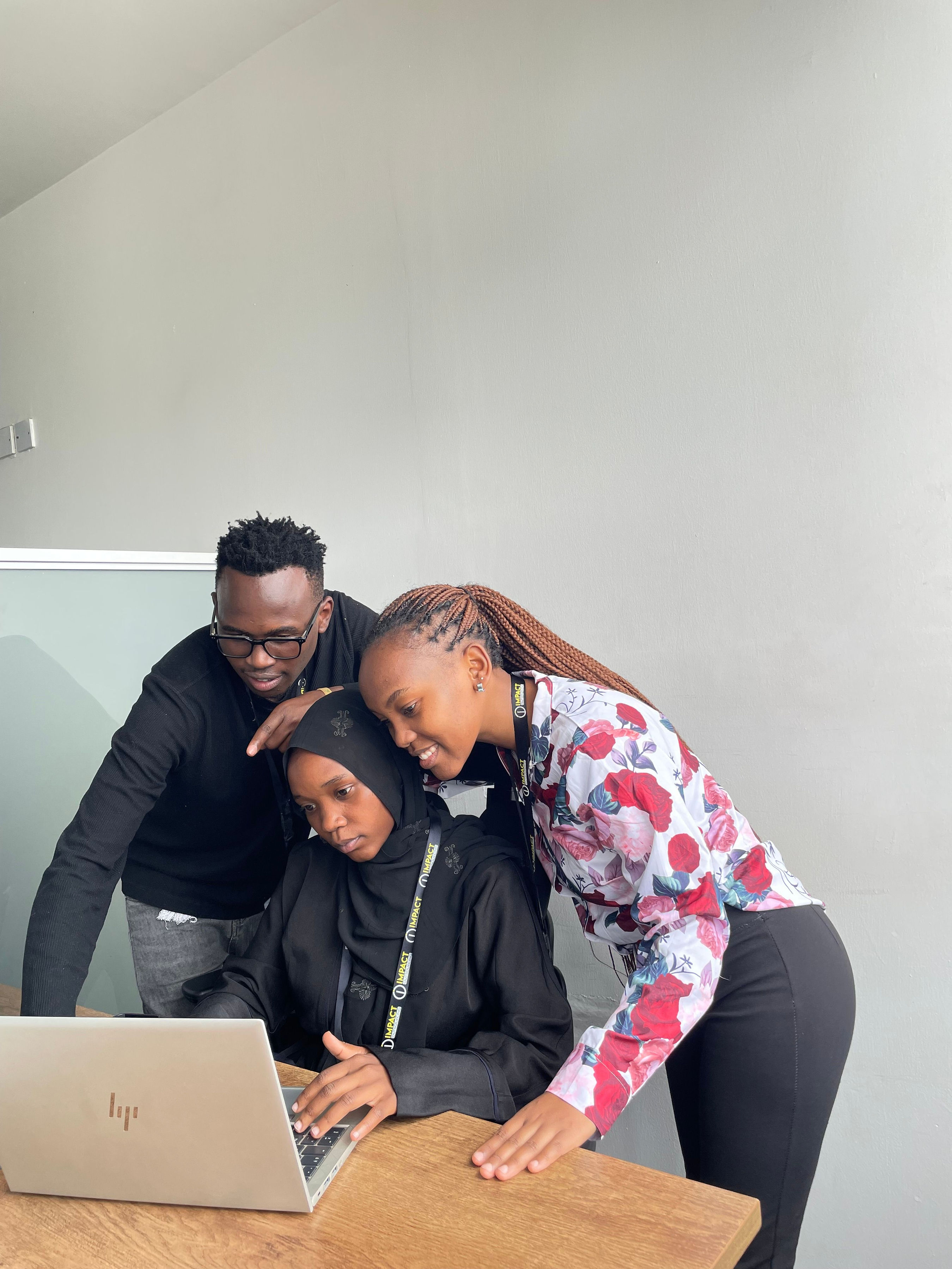 Three Impact Outsourcing team members gathered around a laptop, reviewing work together on the Nairobi delivery floor.