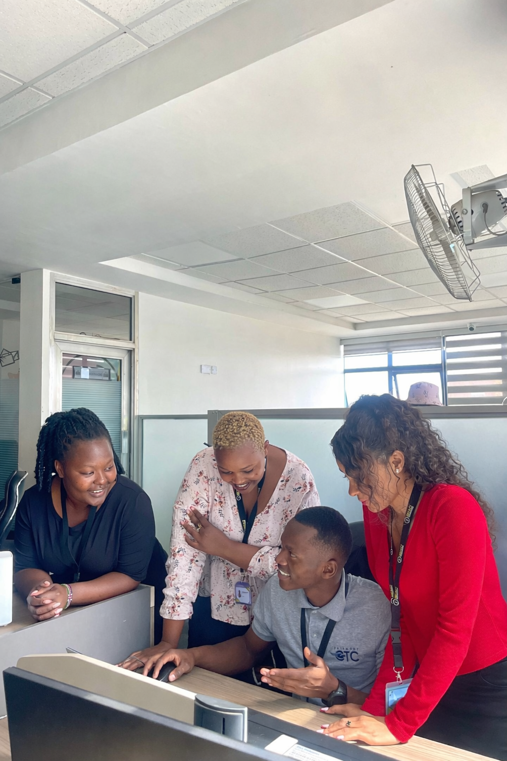 A delivery lead and senior reviewer coaching a team member at his workstation on the Impact Outsourcing delivery floor in Nairobi.