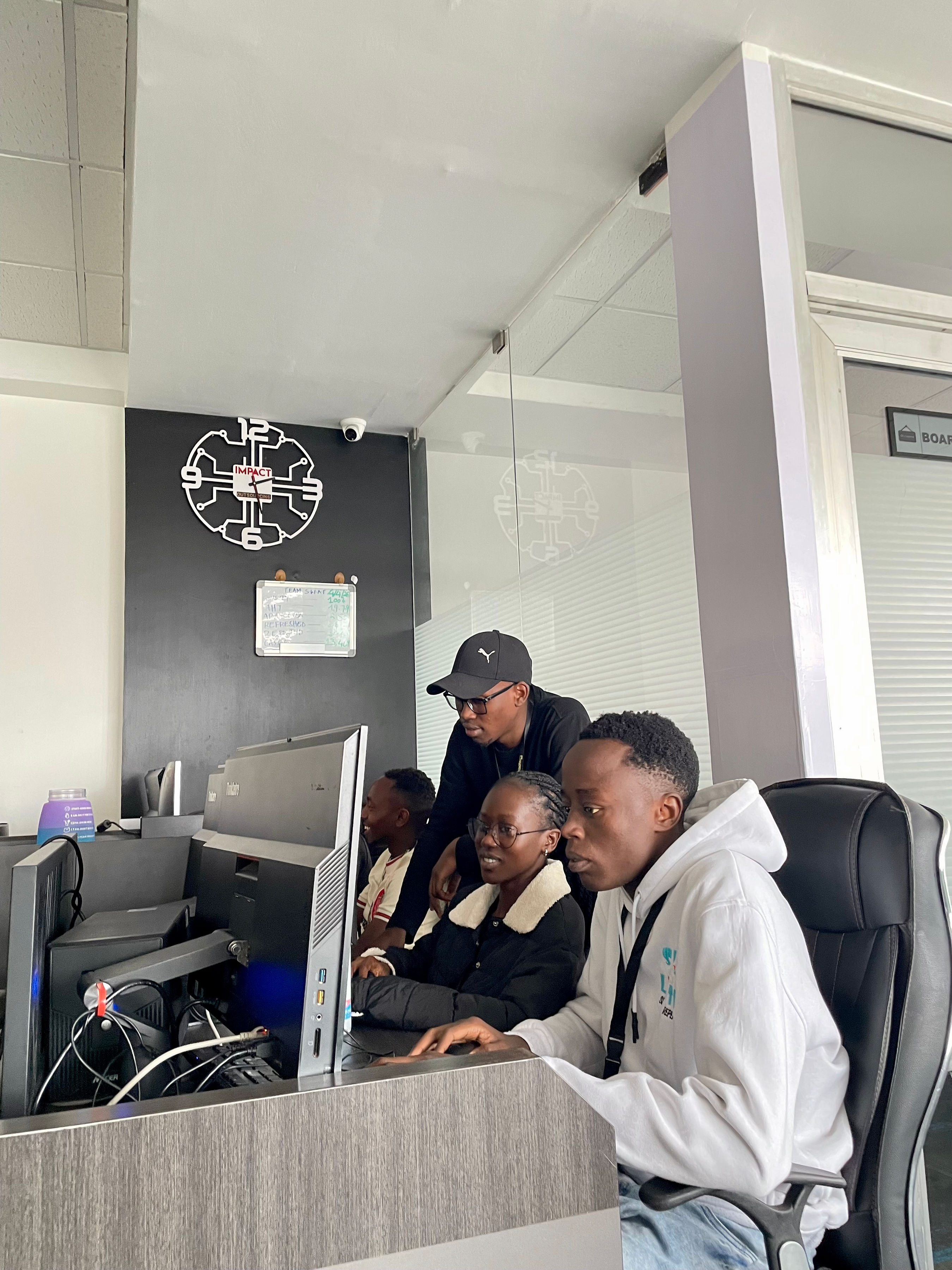 Four Impact Outsourcing team members gathered around a workstation reviewing a live annotation task under the IMPACT clock.